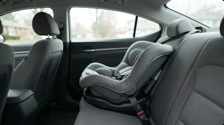 An infant car seat correctly installed rear-facing in the back seat of a car, no people, soft natural daylight